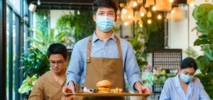 Male waitor bringing food on serving platter with customers in the background.